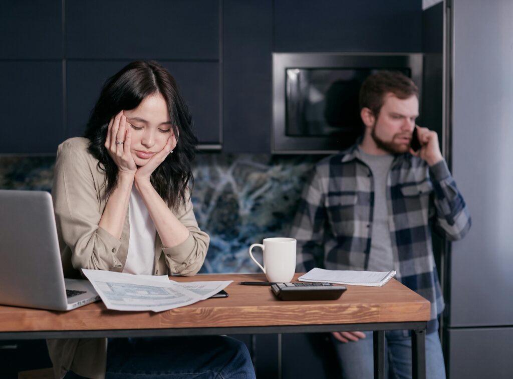 A couple dealing with financial stress, surrounded by bills and a laptop indoors.